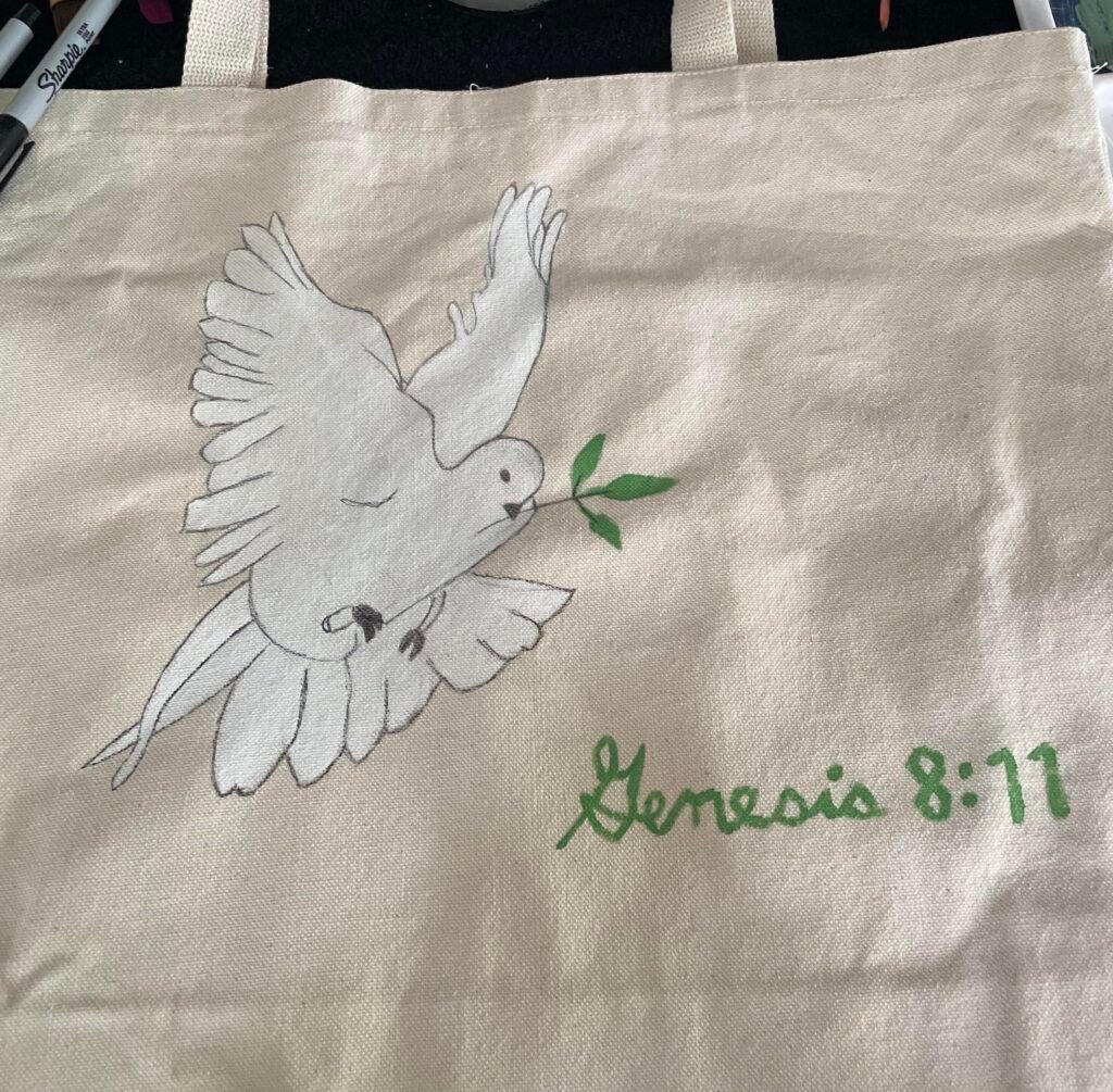 Natural canvas tote bag featuring a hand-painted white dove carrying a green olive leaf, with “Genesis 8:11” written in green lettering.